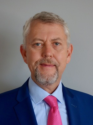 A photo of lawyer Leidereiter in a blue suit with blue shirt and pink tie in front of a gray wall